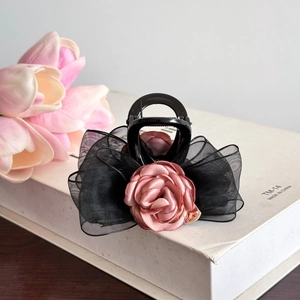 Détail d'une rose en satin rose et nœud en tulle noir sur un support blanc décoratif