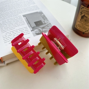 Two-tone acetate hair claws in fuchsia and yellow displayed on a lifestyle desk background