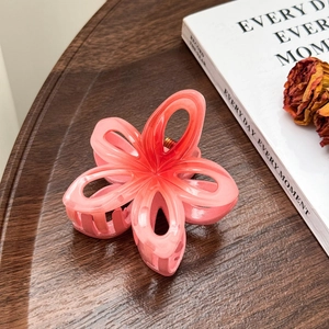 Détail d'une pince à cheveux fleur rose pêche sur un plateau en bois avec un livre rétro