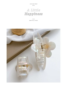 Detail of elegant acetate flower hair claw clip set with pearlescent finish on white fabric