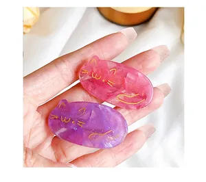 Close-up of glittery resin cat hair clips in pink and purple with gold details