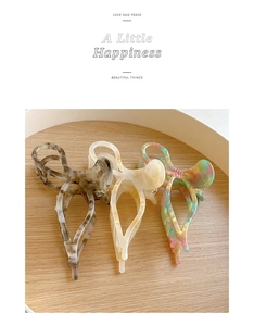 Three elegant resin bow hair claws with marble and colorful patterns on a wooden tray