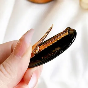 Black oval hair clip with gold metal duckbill clip design and non-slip teeth grip