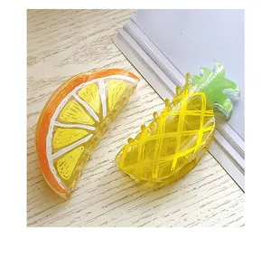Detailed view of large acrylic fruit hair claws in orange slice and pineapple shapes