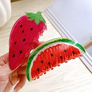 Cute strawberry and watermelon acrylic hair claws shown on a hand with wooden background