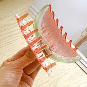 Handheld view of a creative watermelon shaped acrylic hair claw clip with pink and green layers