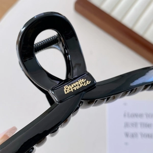 Glänzende schwarze Haarklammer mit goldenem Logo für elegante Damenfrisuren im Alltag