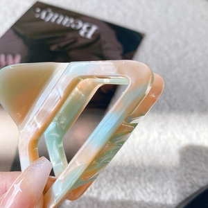 Eleganter Acetat-Haarclip in Dreiecksform mit Marmorierung auf weichem Magazin-Hintergrund
