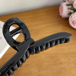 Glossy black large claw clip hair accessory shown on an elegant wooden tabletop