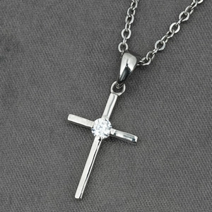 Collier croix argentée polie avec zircon central sur fond en tissu gris élégant