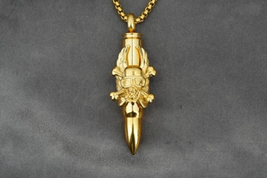 Detailed close-up of golden bullet pendant featuring gothic skull and wings design