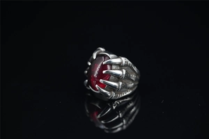 Detailed view of gothic dragon claw ring with deep red oval gemstone on black surface