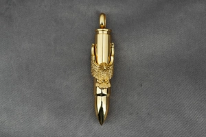 Detail view of gold bullet pendant featuring intricate eagle engraving on gray fabric