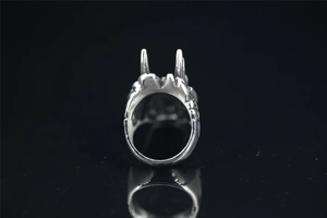 Detailed close-up of a silver punk wolf ring with red eyes on a black reflective surface
