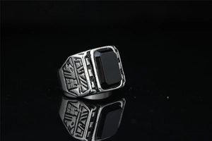 Macro shot of silver signet ring featuring a rectangular black gemstone and relief patterns