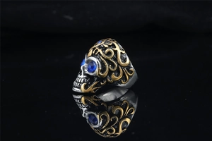 Macro shot of a punk skull ring with gold vine patterns and blue gemstone eyes