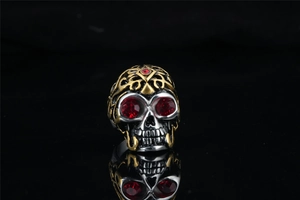 Close-up of hip hop skull ring with red crystals and gold-plated details on dark background