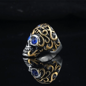 Gothic skull ring in silver and gold tones with blue gemstone eyes on black background