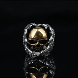 Gothic punk skull ring with golden head and silver wings on a black reflective surface