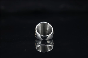 Macro shot of silver signet ring with gold embossed sides on a black reflective surface