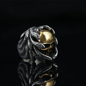 Punk skull biker ring with golden skeleton head and silver wing details on black mirror