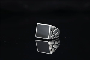 Detail view of rectangular black onyx ring with textured silver-tone relief on band