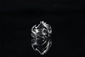Macro detail of silver punk dragon ring with hollow carving on black reflective surface