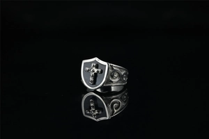 Close-up of vintage punk shield ring featuring a black background and embossed cross detail