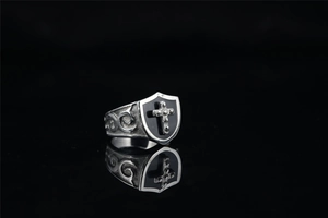 Detailed macro view of retro silver punk shield ring with black cross on a reflective base