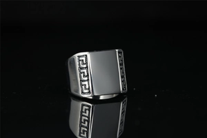 Detailed macro view of men's steel ring with black gemstone and Greek key pattern
