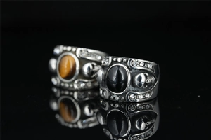 Detail shot of gothic skull rings featuring black onyx and tiger eye stones on black reflective base