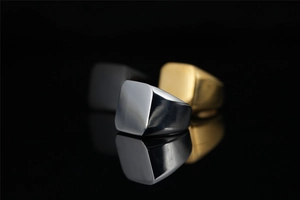Nahaufnahme von quadratischen Siegelringen in Silber, Gold und Mattschwarz mit Metalltextur
