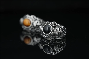 Close-up of vintage gothic skull rings with black agate and amber stones on black glass