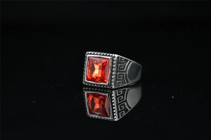 Gros plan d'une bague vintage en acier pour homme avec une pierre rouge carrée et motif grec