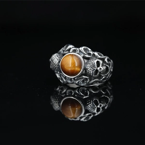 Vintage gothic skull ring for men with round tiger eye stone on a black reflective surface