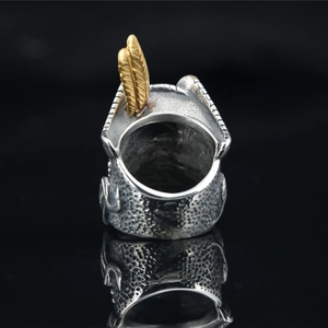 Vintage silver skull ring with gold feather detail and hammered texture on black background