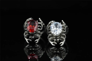 Macro detail of gothic spider rings with red and clear crystals on black reflective surface