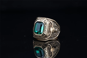 Macro view of emerald-cut green gem and retro floral embossing on gold titanium ring