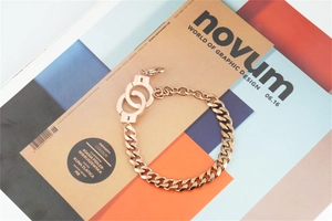 Detailed macro view of rose gold handcuff charm on a curb chain bracelet over a magazine