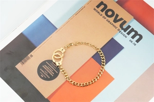 Artistic detail of gold handcuff pendant on a curb chain bracelet over a magazine