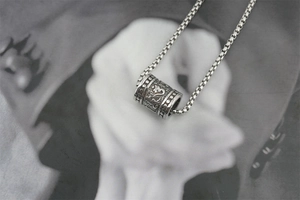 Vue rapprochée du pendentif cylindre rétro en acier avec gravure de mantra sacré