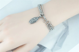 Close-up of silver Cuban link bracelet with Virgin Mary religious pendant and double layer