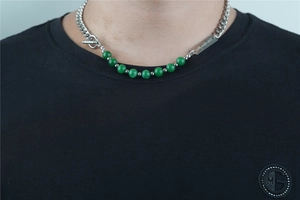 Detailed close-up of chunky titanium steel chain necklace with green beads and T-bar clasp