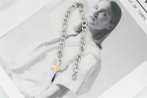 Detail of silver Figaro chain necklace with golden St. Benedict cross pendant on magazine