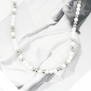 Minimalist pearl and steel bead necklace displayed on a stylish fashion magazine background