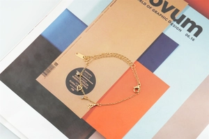 Détail d'un bracelet doré avec breloques tour Eiffel et cœur sur un fond de magazine
