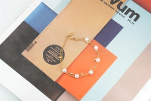 Détail d'un bracelet double couche perlé doré avec fermoir mousqueton sur un magazine