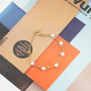 Bracelet double couche en acier titane doré avec perles blanches sur fond géométrique