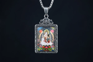 Detail showing an intricate filigree Thangka Buddha pendant on a stainless steel chain
