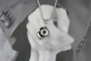 Close-up of vintage silver camera pendant with detailed lens on a box chain necklace